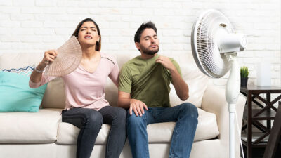 Ventiladores Profeco: Hombre y mujer sentados en un sillón acalorados frente a ventilador encendido