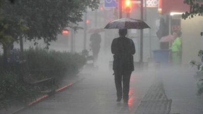 Persona caminando bajo una fuerte lluvia y cubriéndose con un paraguas.
