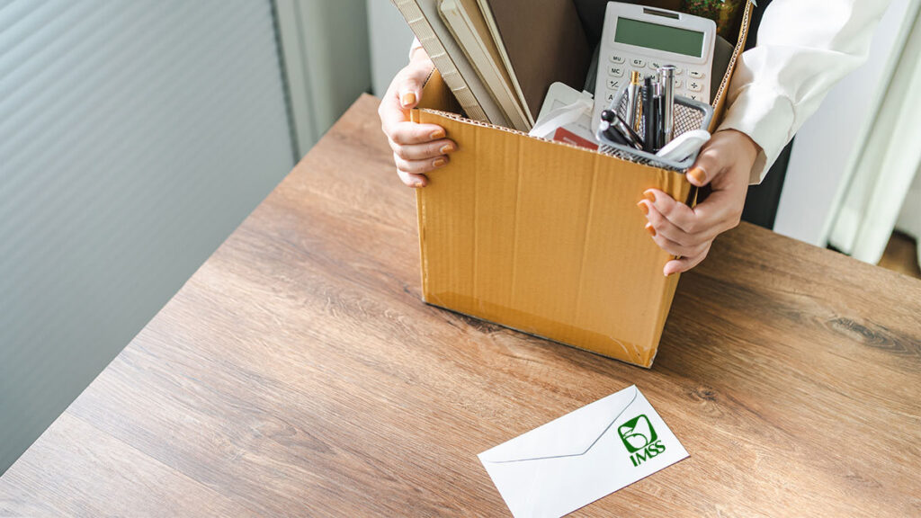 Afore semanas cotizadas retiro parcial: Persona con sosteniendo una caja con cosas de oficina sobre un escritorio con un sobre con el logo del IMSS