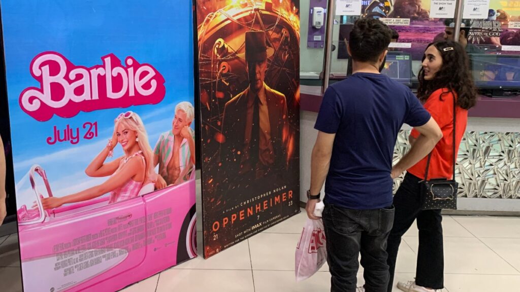 Pareja viendo un cartel de Barbie y Oppenheimera la entrada de un cine en Pakistán