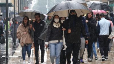 Personas cubriéndose de la lluvia abrigados y con paraguas en calles del Centro Histórico de la CDMX