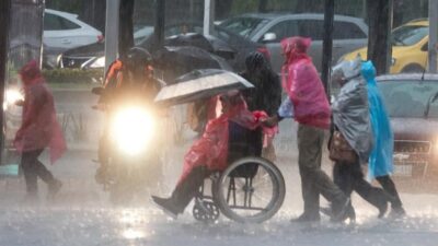 Personas caminan bajo la lluvia fuerte cubiertas con plásticos y paraguas