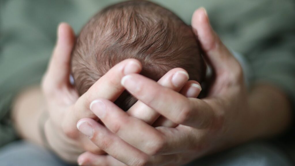 Madre cargando a bebé con las manos en su cabeza.