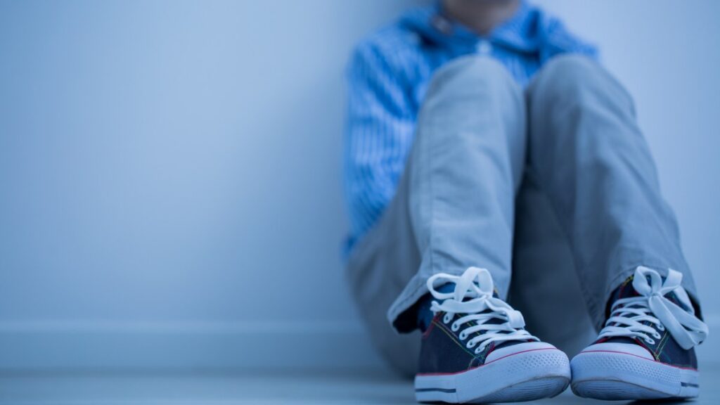 Niño triste sentado recargándose en una pared