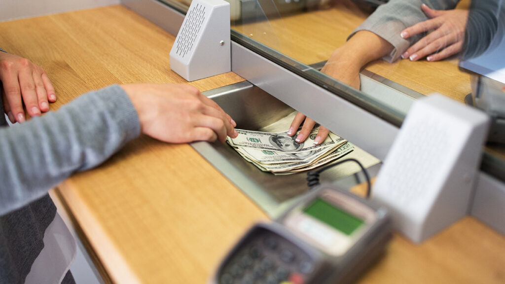 Remesas mayo: persona dando dólares a una cajera a través de ventanilla bancaria