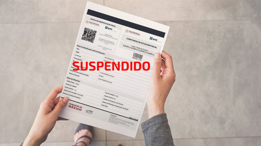 Persona agarrando una Constancia de Situación Fiscal del SAT con "suspendido" escrito en letras rojas
