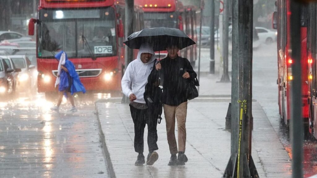 Dos jóvenes caminan bajo la lluvia en la avenida Reforma de la CDMX