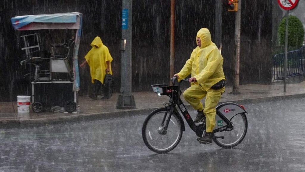 Un hombre en bicicleta con impermeable amarillo circula en una calle bajo la lluvia en la CDMX