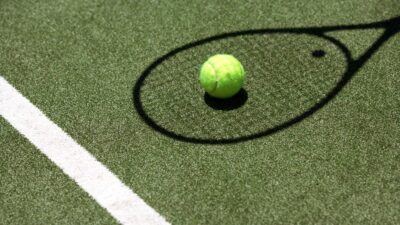 Pelota de tenis sobre el césped bajo una sombra de una raquera