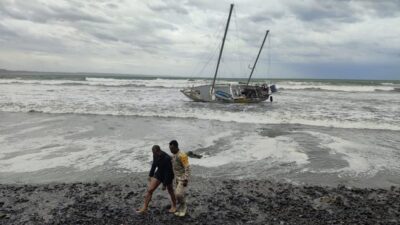 Elemento del ejército ayuda a un turista en una playa mexicana. De fondo una embarcación luce dañada