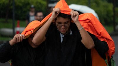 Jóvenes se cubren de la lluvia con una chamarra color naranja en una calle de la CDMX