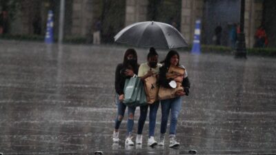 Mujeres cargan bolsas y se cubren de la lluvia con un paraguas