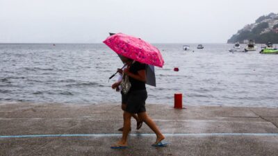 Mujeres caminan con paraguas rosa a la orilla del mar y bajo una fuerte lluvia