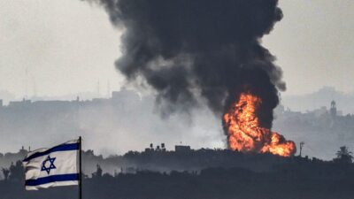 Bombardeo en la Franja de Gaza en las cercanías de Israel, cuya bandera ondea en el primer plano