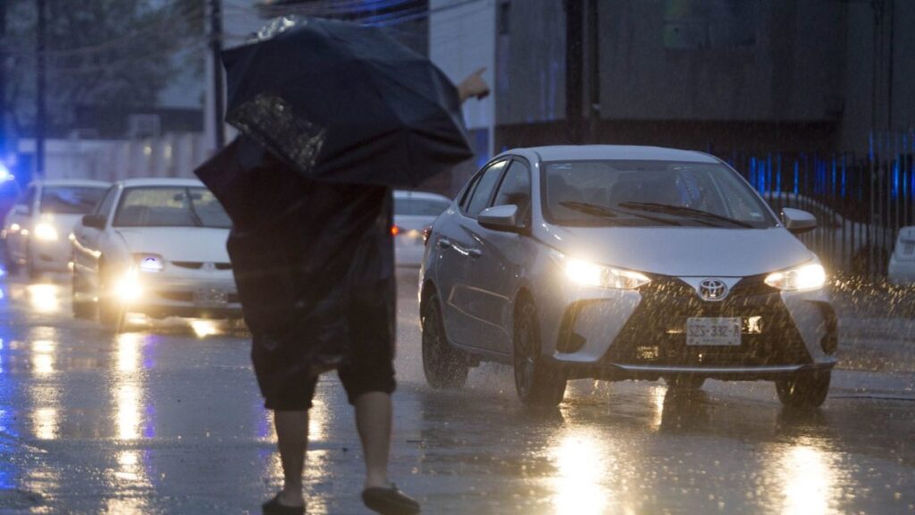 Una persona con paraguas bajo una fuerte lluvia hace la parada a un taxi