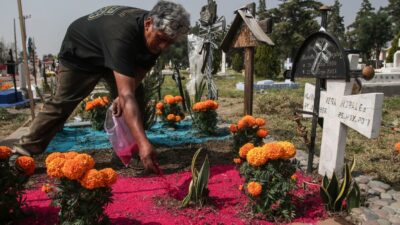 Hombre limpia y adorna una tumba en un panteón de la Ciudad de México