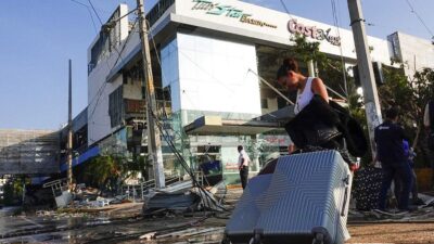 Turista con maletas afuera de central de autobuses de Acapulco, ciudad que luce con destrozos