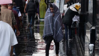 Hombre se cubre del frío y la lluvia con una cobija en una calle