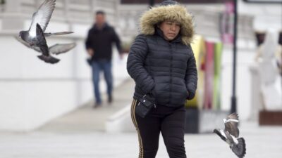 Mujer con chamarra y capucha camina bajo el frío