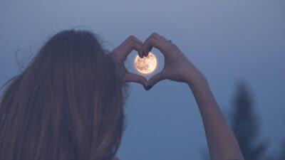 Mujer hace la forma del corazón con sus manos apuntando a la Luna