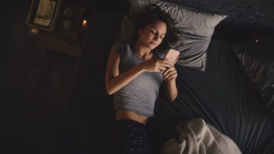 Mujer revisa el celular acostada en su cama