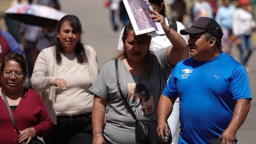 Gente camina sobre una calle, mientras una mujer se cubre el rostro para cuidarse del sol