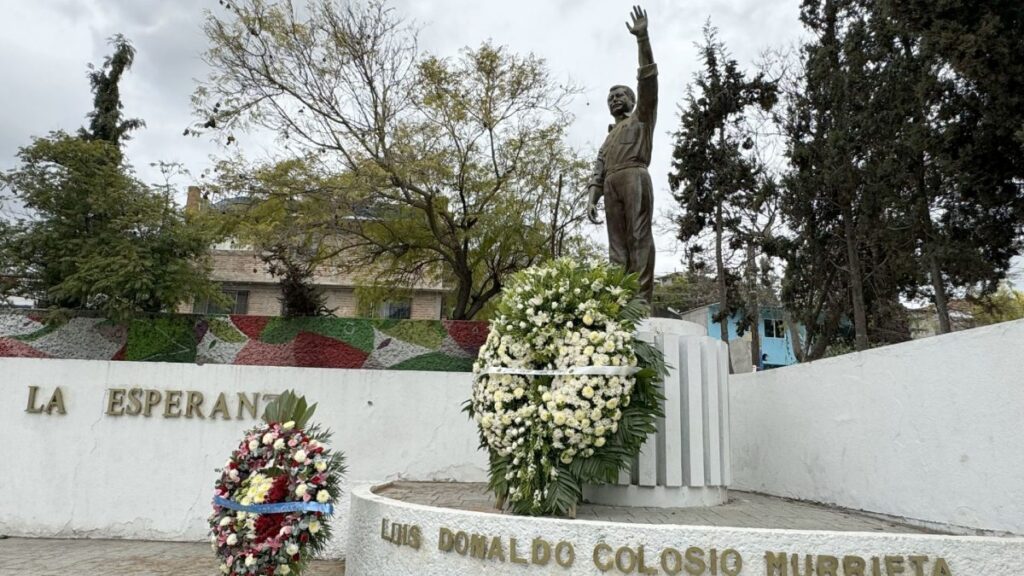 Estatua de Luis Donaldo Colosio rodeada de arreglos florales en su aniversario luctuoso