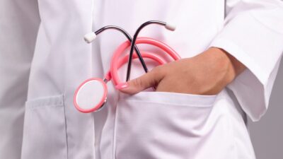Doctor con estetoscopio de color rosa en una de las bolsas de su bata blanca