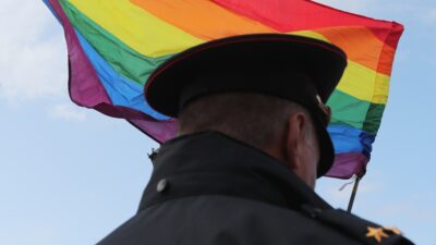 Soldado de Rusia de espaldas con la cara hacia una bandera arcoíris de la comunidad LGBT