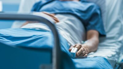 Persona enferma en cama de hospital con oxímetro en el dedo.