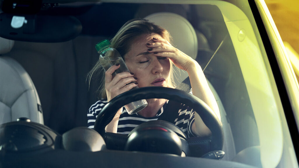 Mujer manejando su auto en el calor, enfriándose la cara con una botella de agua