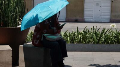 Mujer se cubre del calor con una sombrilla, sentada en alguna parte de la CDMX
