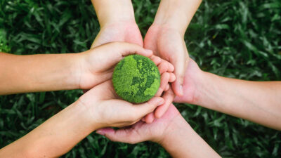 Manos de tres personas sobre pasto sosteniendo un mundo verde