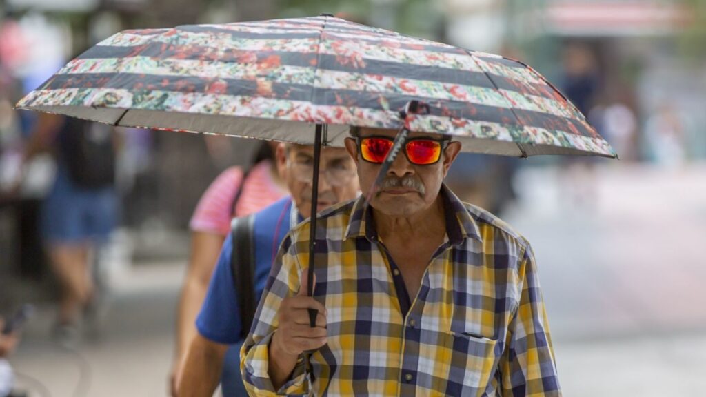 Hombre con sombrilla y lentes oscuros caminando en una calle soleada ola de calor